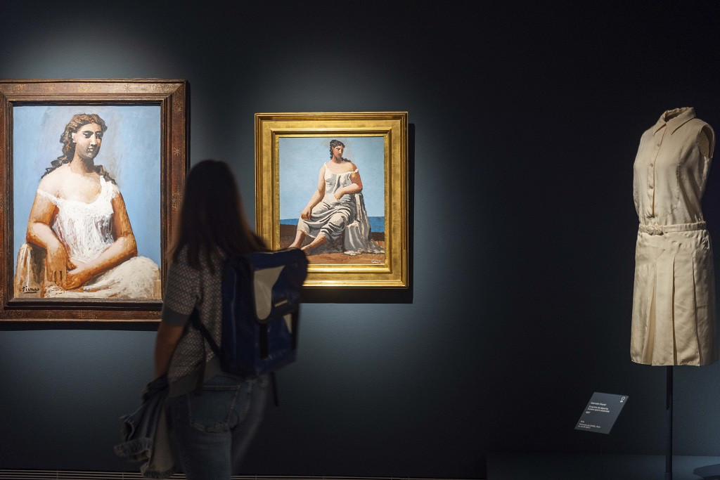 Una mujer observa en una de las salas de ‘Picasso / Chanel’ las distintas versiones de ‘Mujer frente al mar’ frente a un diseño de Chanel. MUSEO THYSSEN-BORNEMISZA