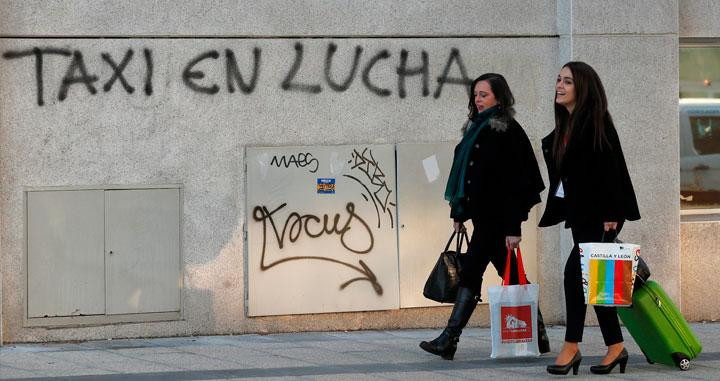 Dos viajeras pasan ante un grafiti que reza Taxi en lucha en Barcelona / EFE