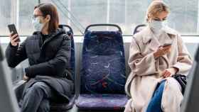 Dos mujeres con mascarilla y el móvil en la mano en un autobús / FREEPIK