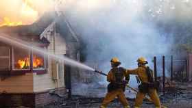 Dos bomberos intentan sofocar el fuego que quema una casa en San Bernardino, California. / EFE