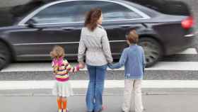 Un vehículo pasa delante de una madre con sus dos hijos /  FUNDACION LA CAIXA