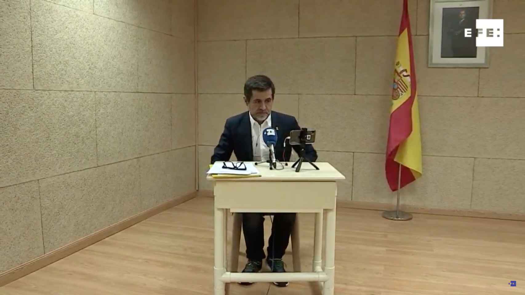 Jordi Sànchez, a punto de empezar la rueda de prensa en Soto del Real con la bandera de España y la foto del Rey detrás / EFE