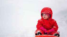 Un niño disfruta de la nieve con un trineo y abrigo rojo / PEXELS