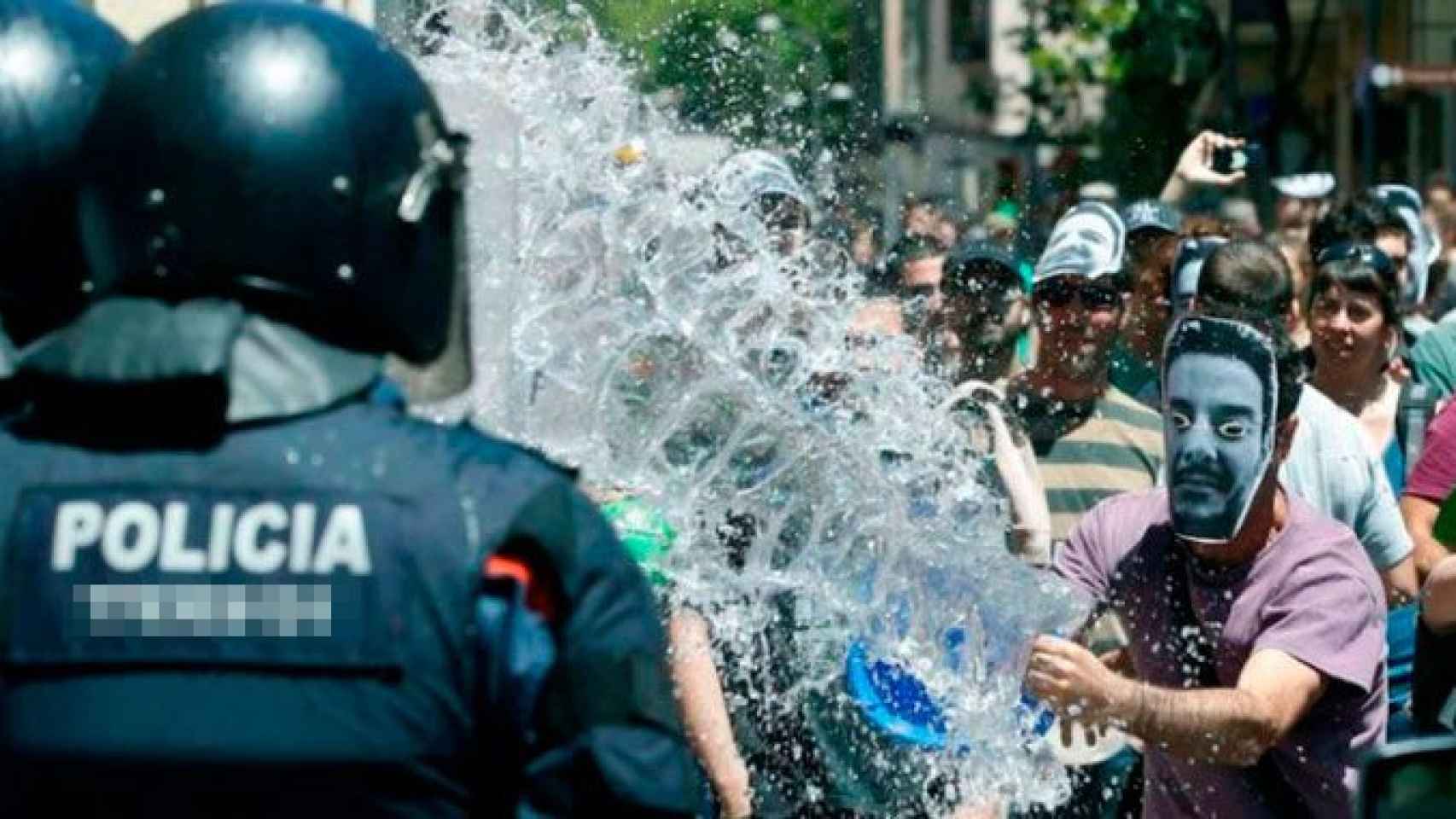 Un okupa del Banc Expropiat de Gràcia lanza un cubo de agua a un agente de los Mossos d'Esquadra / EFE