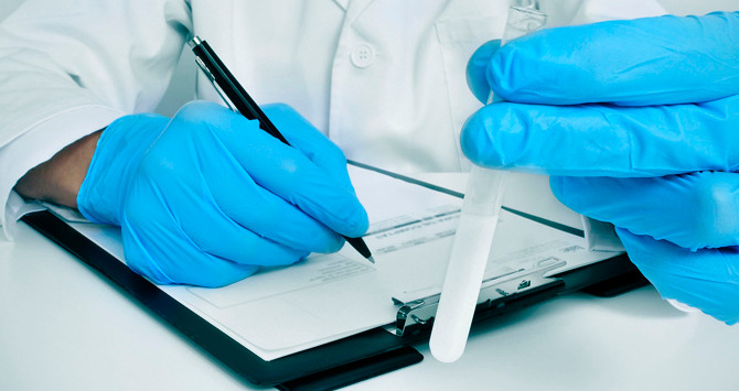 Un médico rellena un formulario con una proveta en la mano