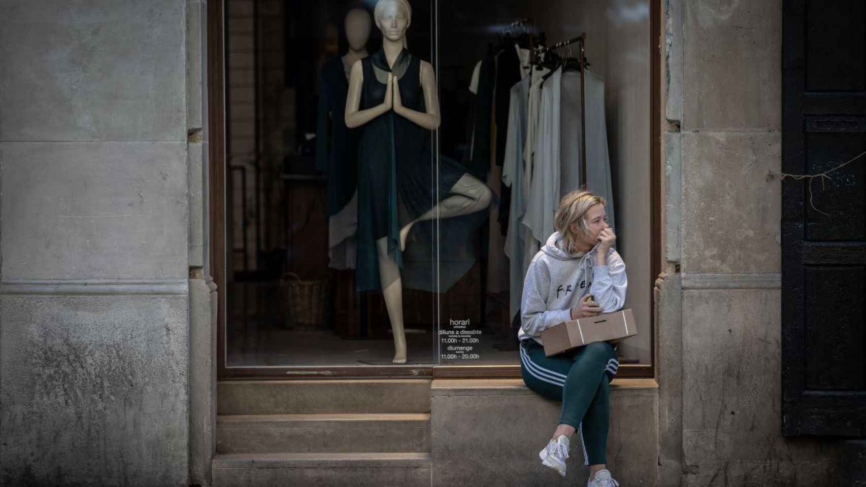 Una mujer sentada ante un escaparate de una tienda de ropa cerrada por no ser comercio esencial / EP
