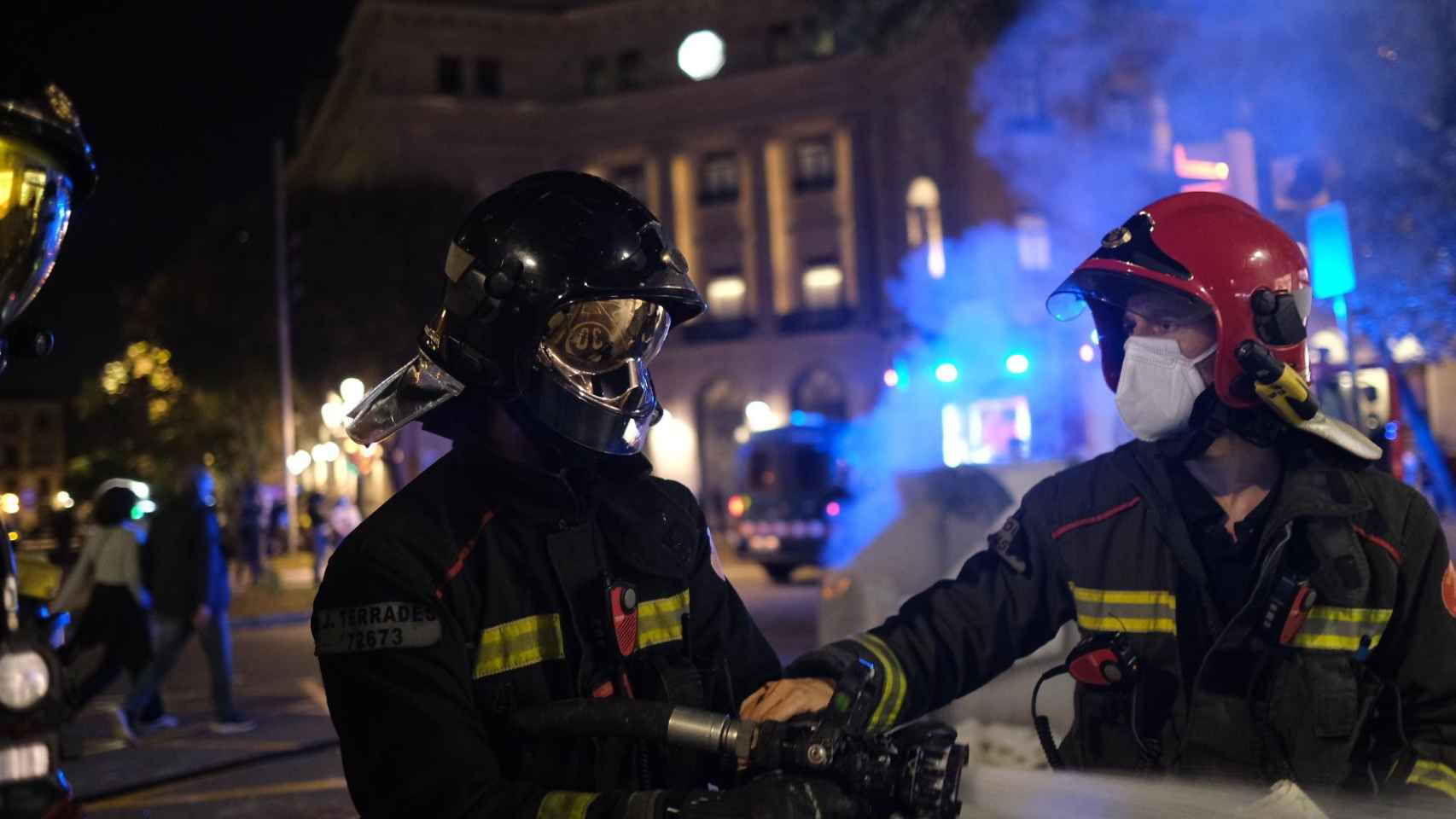 Dos bomberos luchan contra el fuego en el centro de Barcelona durante los disturbios generados tras una manifestación contra las restricciones del Govern