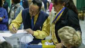 Dos trabajadores de Correos entregan el voto por correo en una mesa electoral / EFE