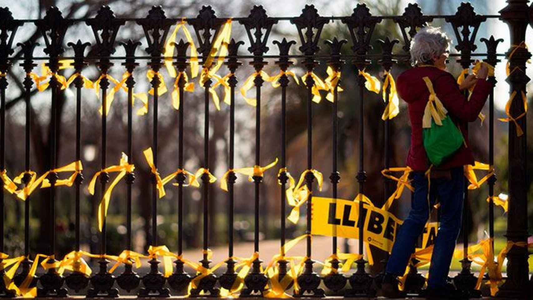Una mujer coloca lazos amarillos en la verja del parque de la Ciutadella, donde se encuentra el Parlament, en referencia al conflicto catalán, uno de los riesgos mundiales de 2018 / EFE
