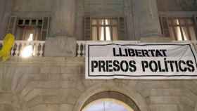 Un lazo amarillo, como el usado por una científica en una base militar, y la pancarta por la libertad de los presos en la fachada del Ayuntamiento / CG