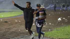 Dos hombres y un niño huyendo de los disturbios en un partido de fútbol en el estadio Kanjuruhan de Malang, en Indonesia, que han causado más de un centenar de muertos /  EFE - Sandi Sadewa