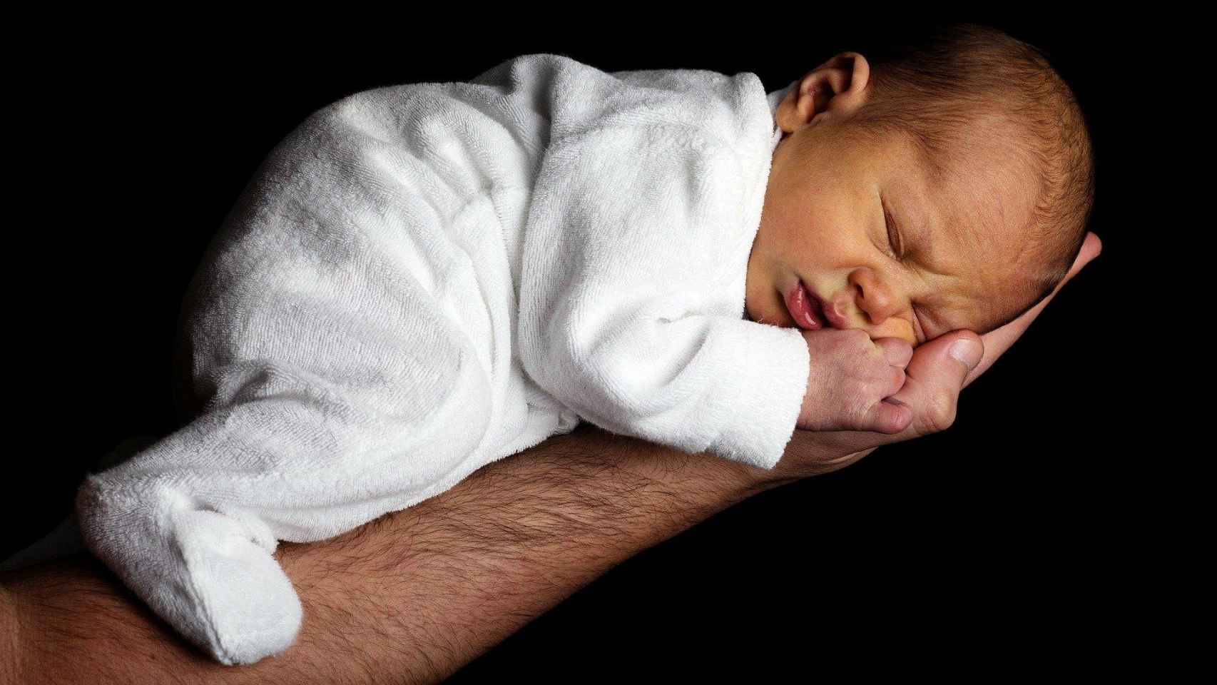 Un bebé recién nacido sobre la palma de la mano de su padre / CG