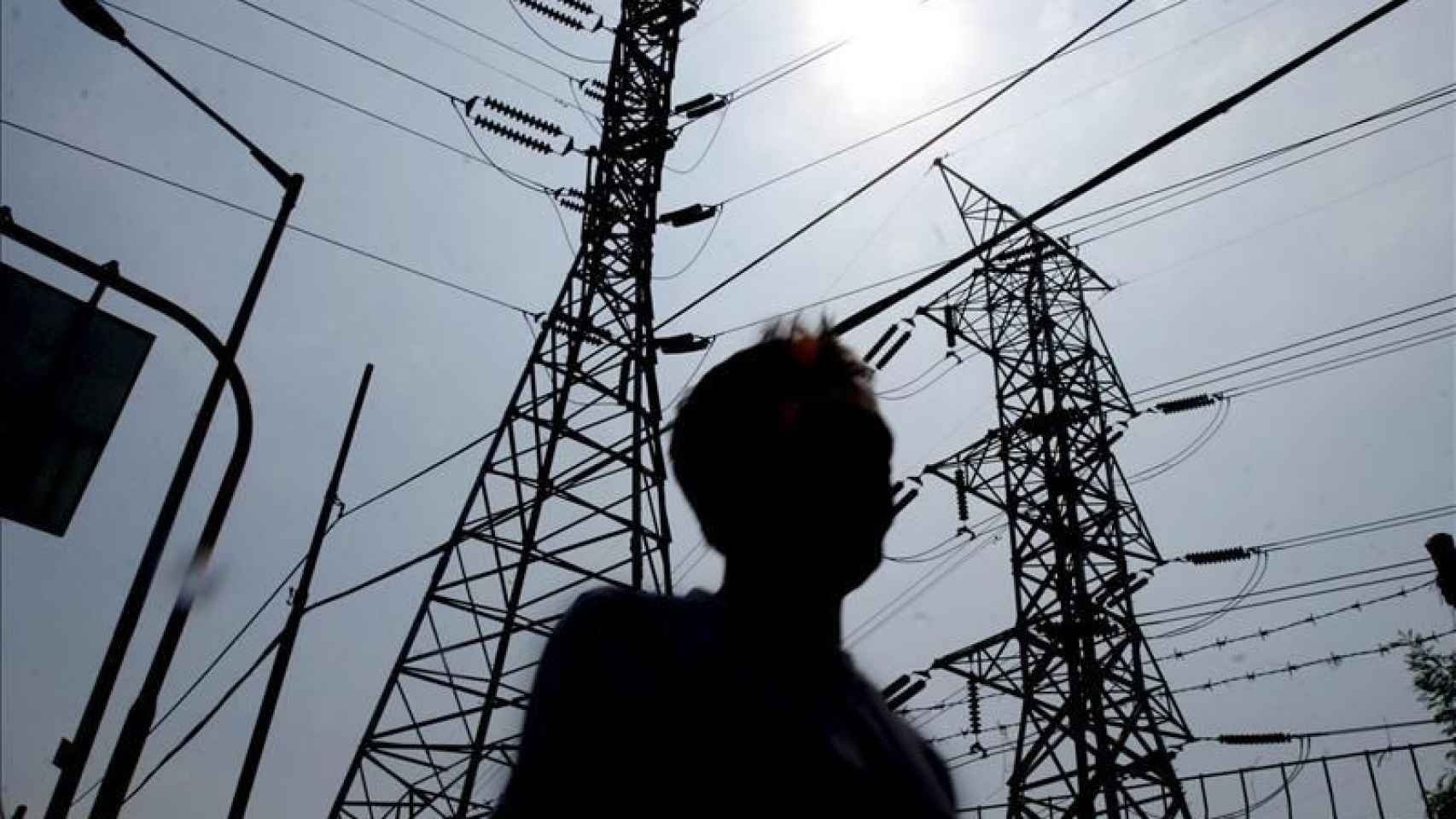 Un hombre pasa por delante de unas torres de electricidad, cuya factura mantiene la subida de los precios en España en el 2,2% en agosto / EFE