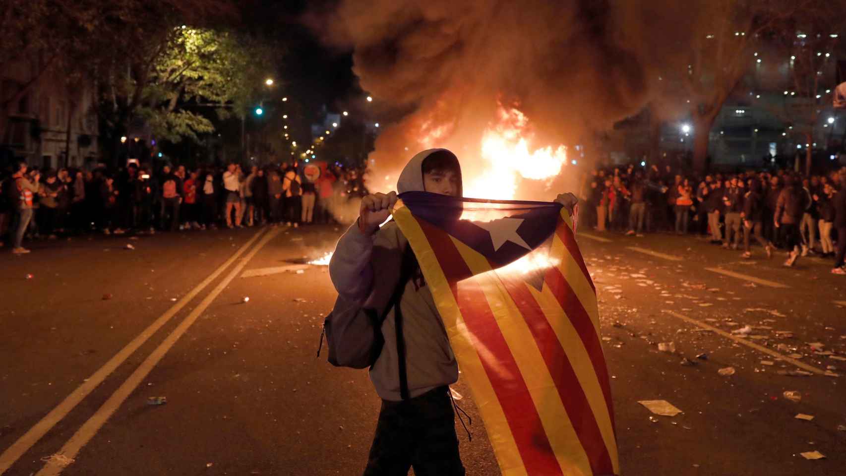 Un radical del independentismo exhibe la estelada mientras arde en llamas un contenedor al lado del Camp Nou / EFE