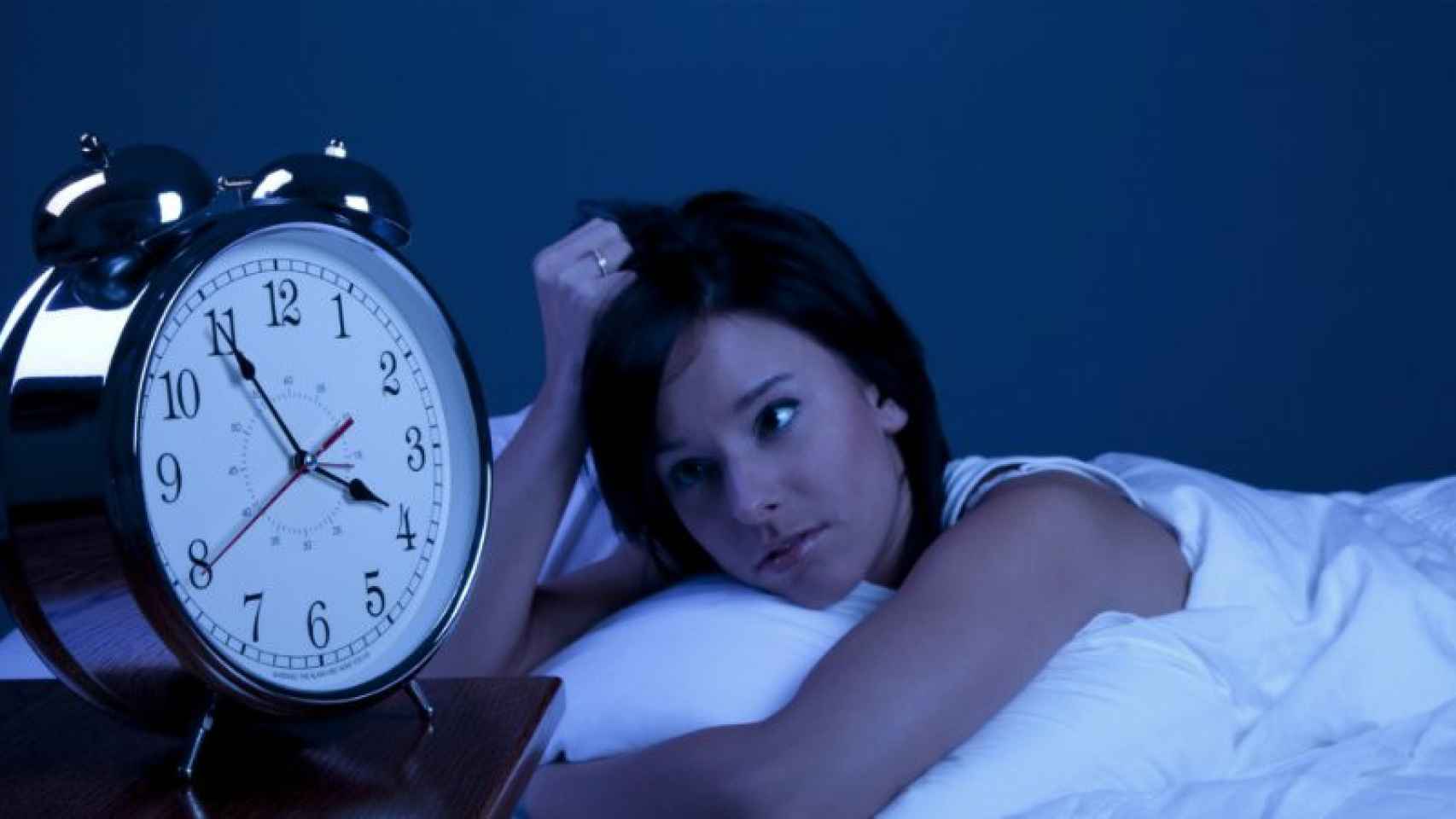 Una mujer en la cama que mira el reloj para saber la hora que es.
