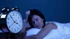 Una mujer en la cama que mira el reloj para saber la hora que es.