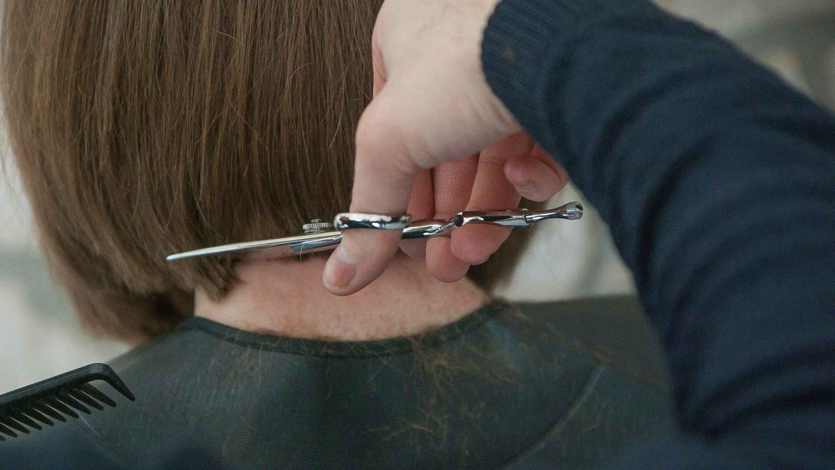 Un peluquero le corta el pelo a una mujer con unas tijeras / CG