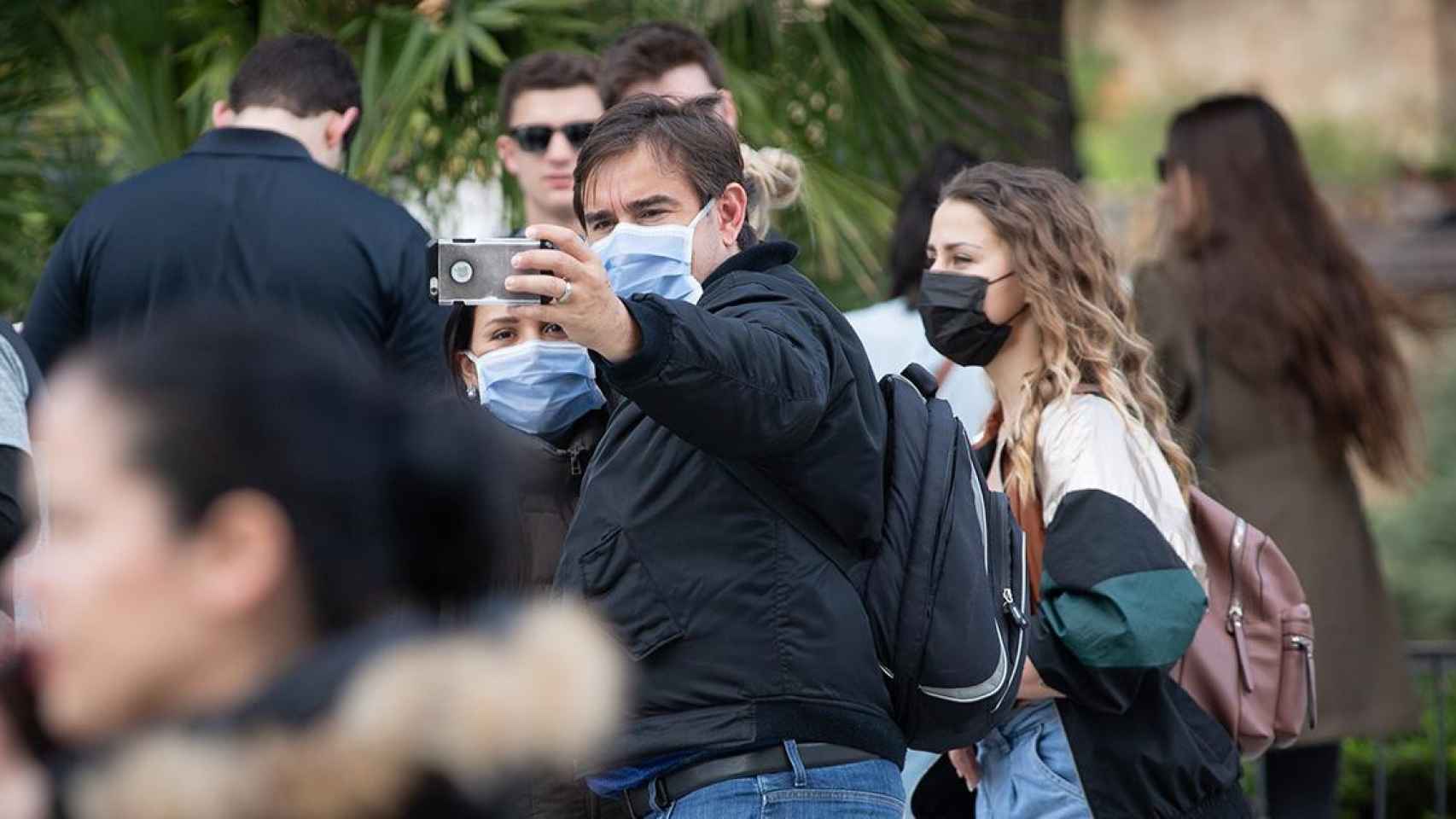 Dos personas se hacen un selfie y otra camina en una zona cercana a la Sagrada Familia con mascarillas contra el coronavirus antes del estado de alarma / EP