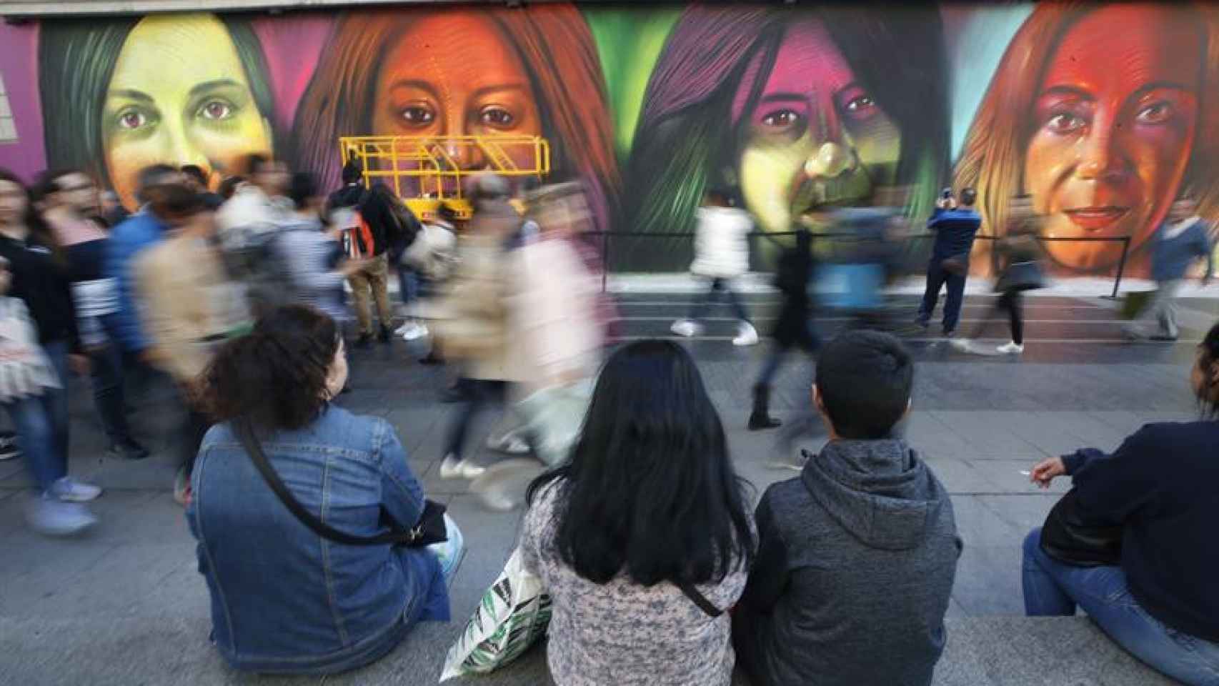 Jóvenes sentados ante un mural feminista / EFE