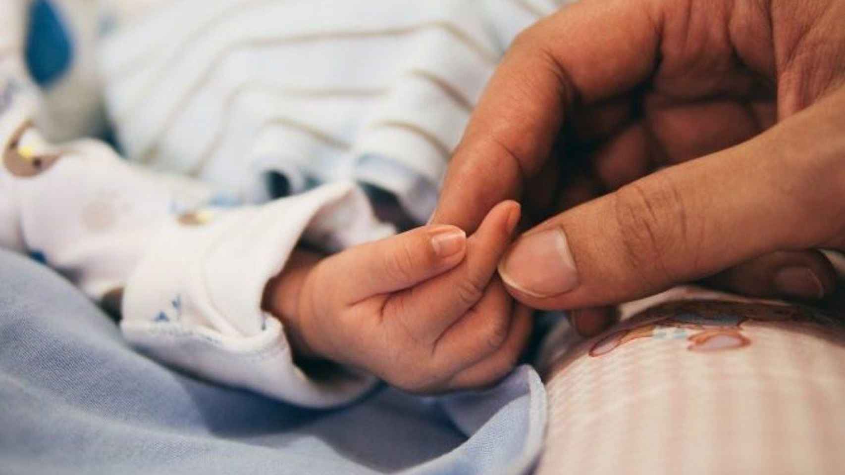 Una persona coge la mano de un bebé / EP