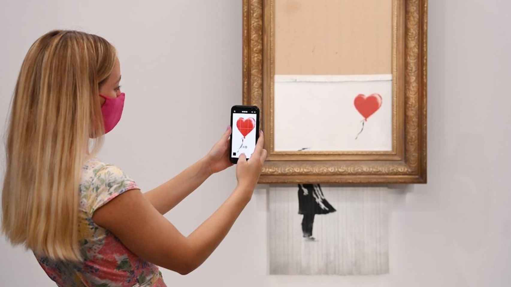 Una empleada de la galería toma una foto de la obra de Banksy que el propio artista destruyó parcialmente en 2018 / FACUNDO ARRIZABALAGA - EFE
