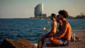 Imagen de tres jóvenes en un espigón de Barcelona con el hotel W Barcelona al fondo / EFE