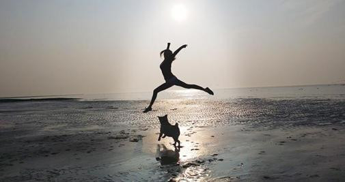 Una mujer jugando con su perro en la playa / EYEEM