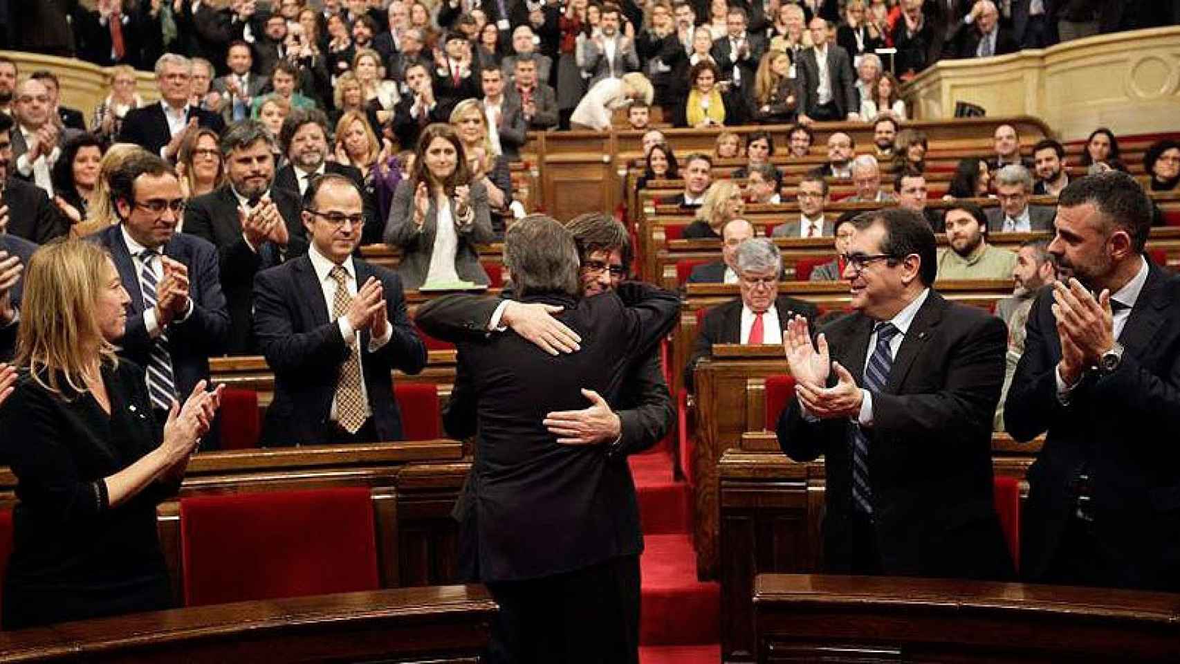 Artur Mas (de espaldas), saluda a Carles Puigdemont, poco antes de comenzar el pleno del Parlament en el que se ha debatido la investidura de Puigdemont.