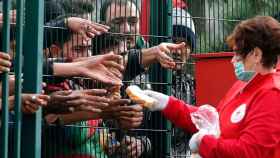 Una trabajadora de la Cruz Roja ofrece pan a los refugiados tras una valla.