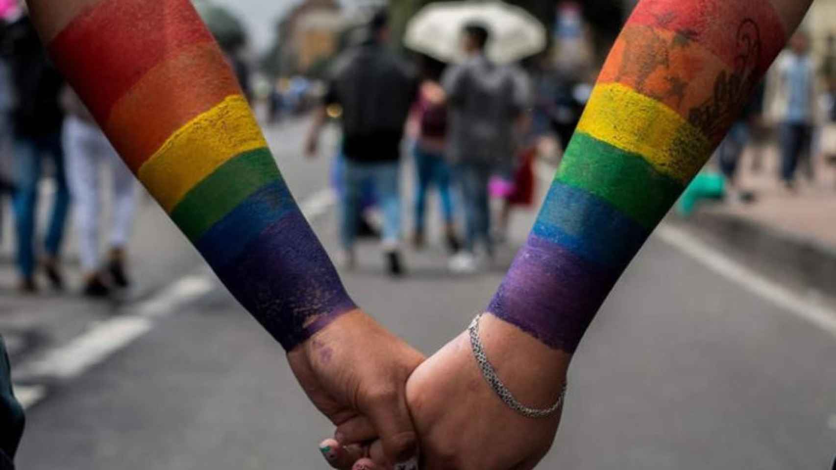 Dos personas con la bandera LGTBI dibujada en el brazo se dan la mano / EFE