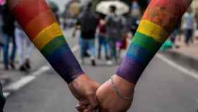 Dos personas con la bandera LGTBI dibujada en el brazo se dan la mano / EFE