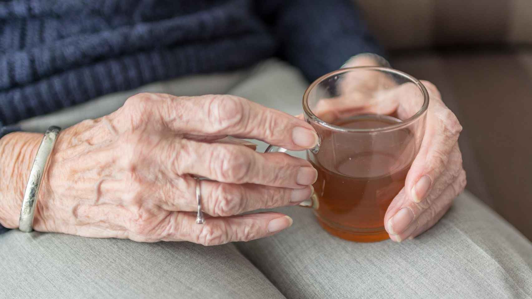 Las manos de una anciana que sujeta un vaso con té / CG