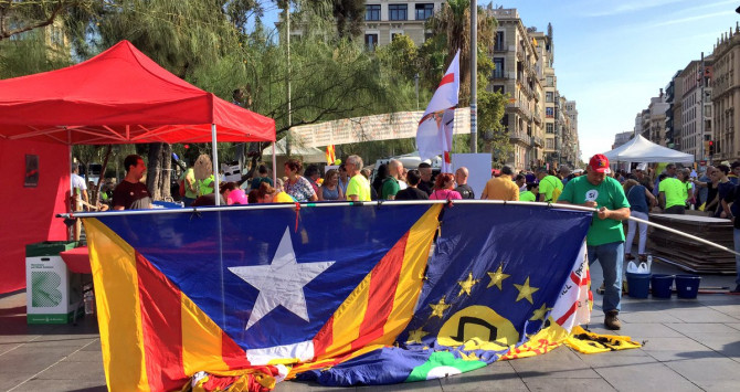 Un hombre trata de levantar una enorme bandera estelada en la plaza Universitat durante la 'empapelada' en toda Cataluña organizada por la ANC y Òmnium Cultural / CG