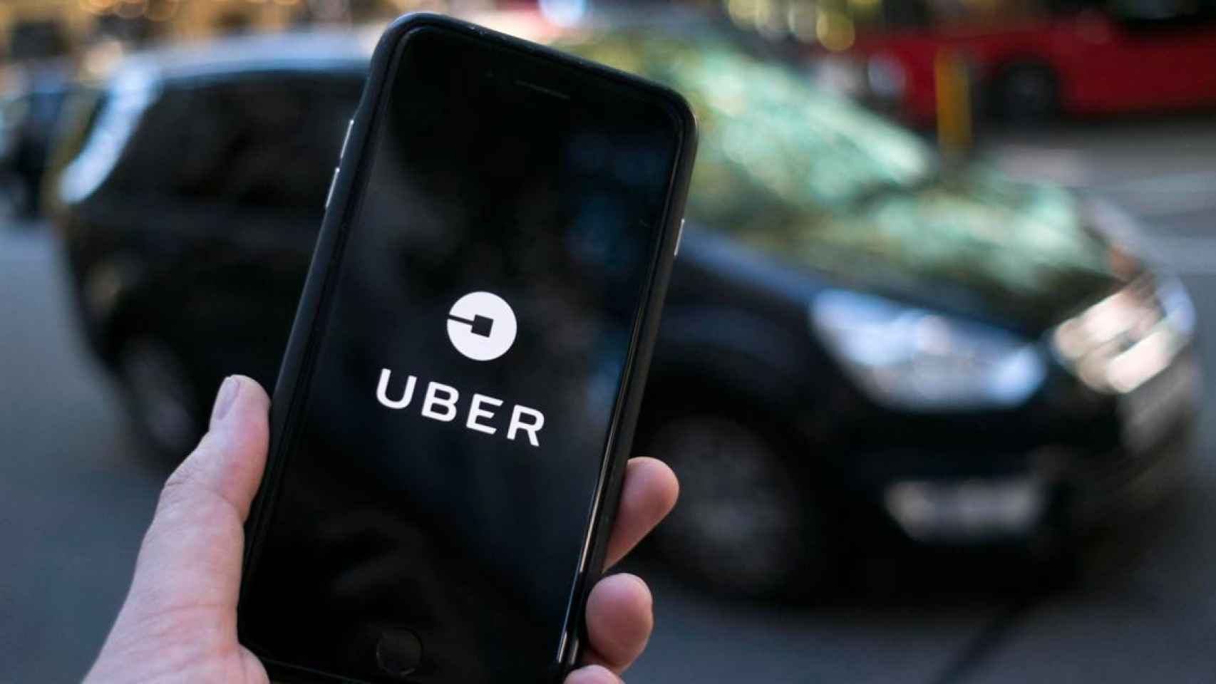Imagen de un vehículo de Uber ante un móvil con la aplicación intermediaria de transporte / CG