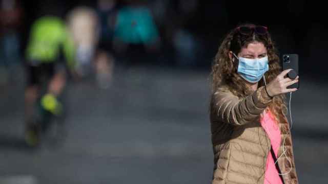 Una mujer usa su smartphone mientras pasea por la calle con mascarilla / EP