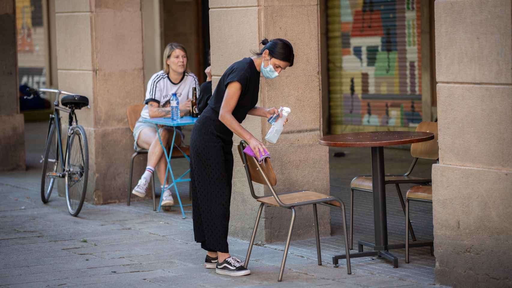 Una camarera limpia varias sillas y una mesa de la terraza de un bar de Barcelona, durante la desescalada de mayo de 2020 / DAVID ZORRAKINO - EUROPA PRESS