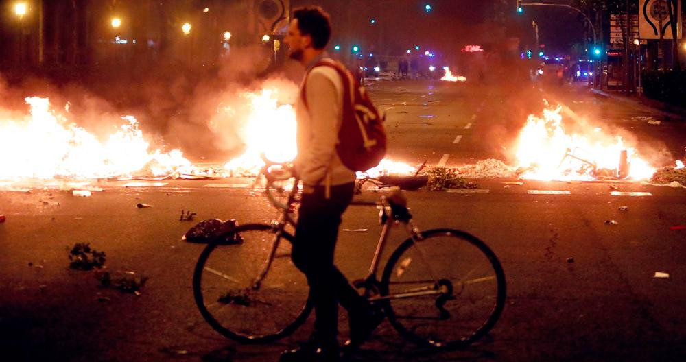 Un joven pasea con su bicicleta, en Barcelona, junto a las barricadas en llamas de una manifestación independentista / C.G.