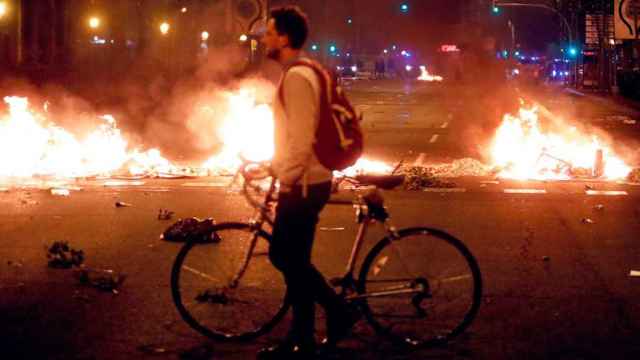 Un joven pasea con su bicicleta, en Barcelona, junto a las barricadas en llamas de una manifestación independentista / C.G.