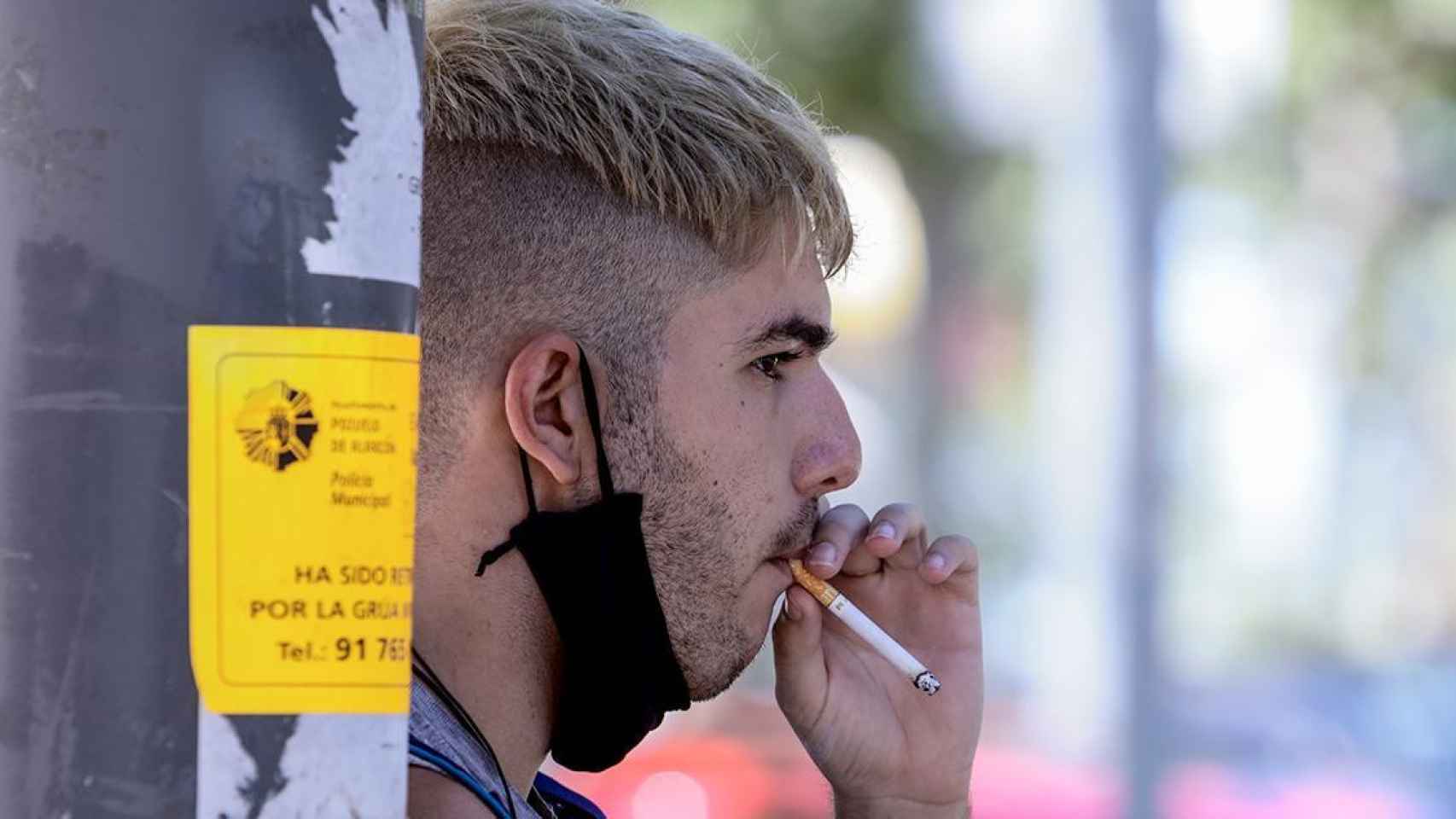 Un joven con la mascarilla bajada para poder fumar / EP