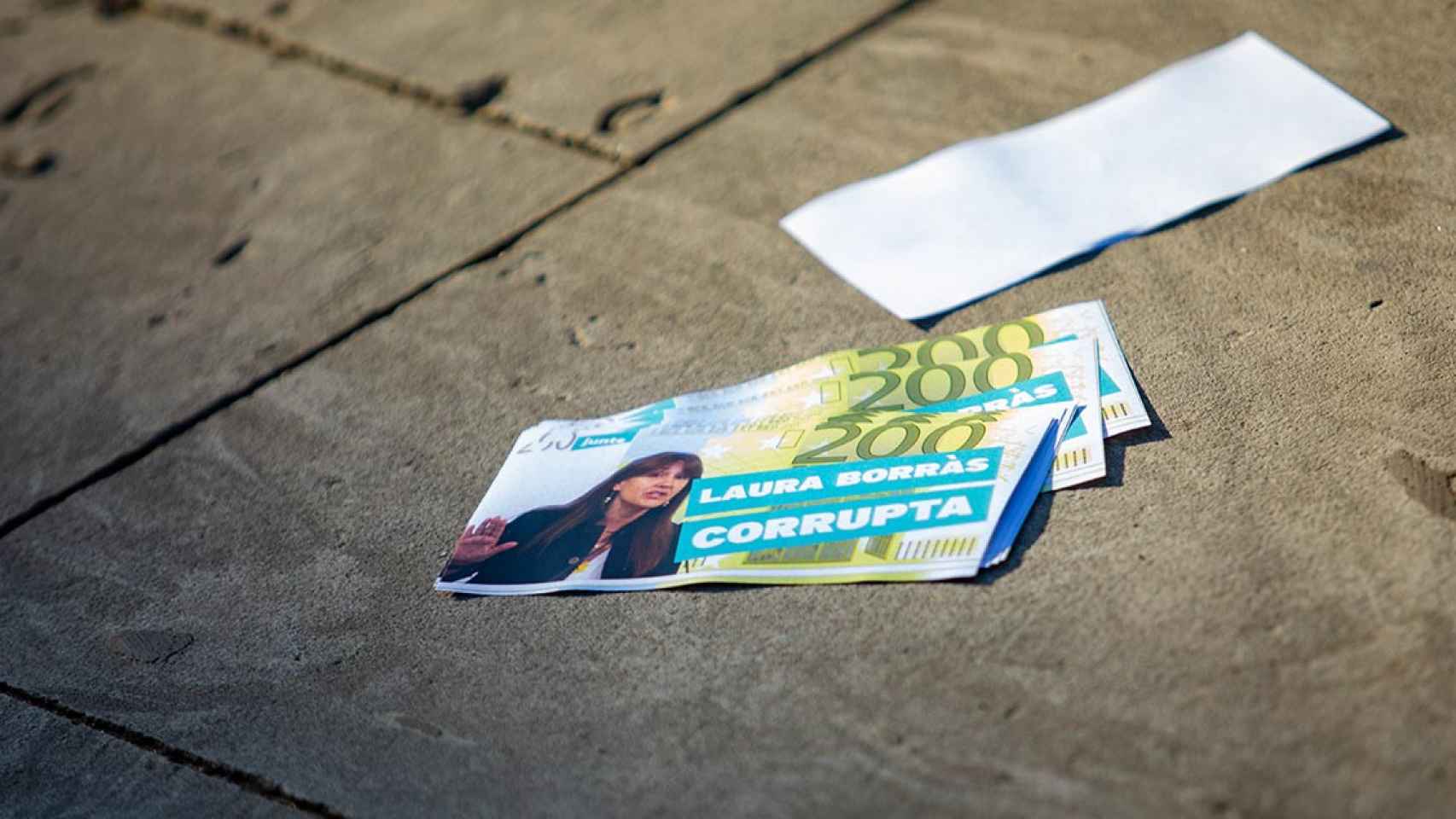 Una persona lanza billetes falsos de 200 con el mensaje 'Laura Borràs corrupta' / EUROPA PRESS