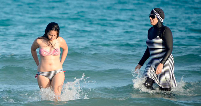 Una mujer se baña con un burkini frente a otra, que lo hace en bikini / AFP