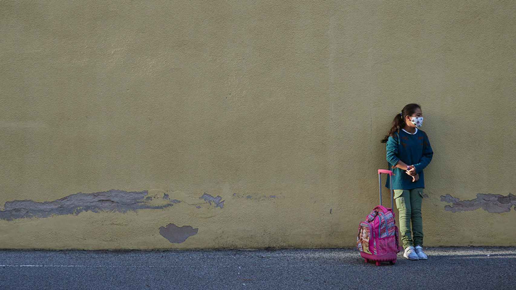 Una niña sola apoyada en la pared mientras espera a sus padres a la salida del colegio / EUROPA PRESS