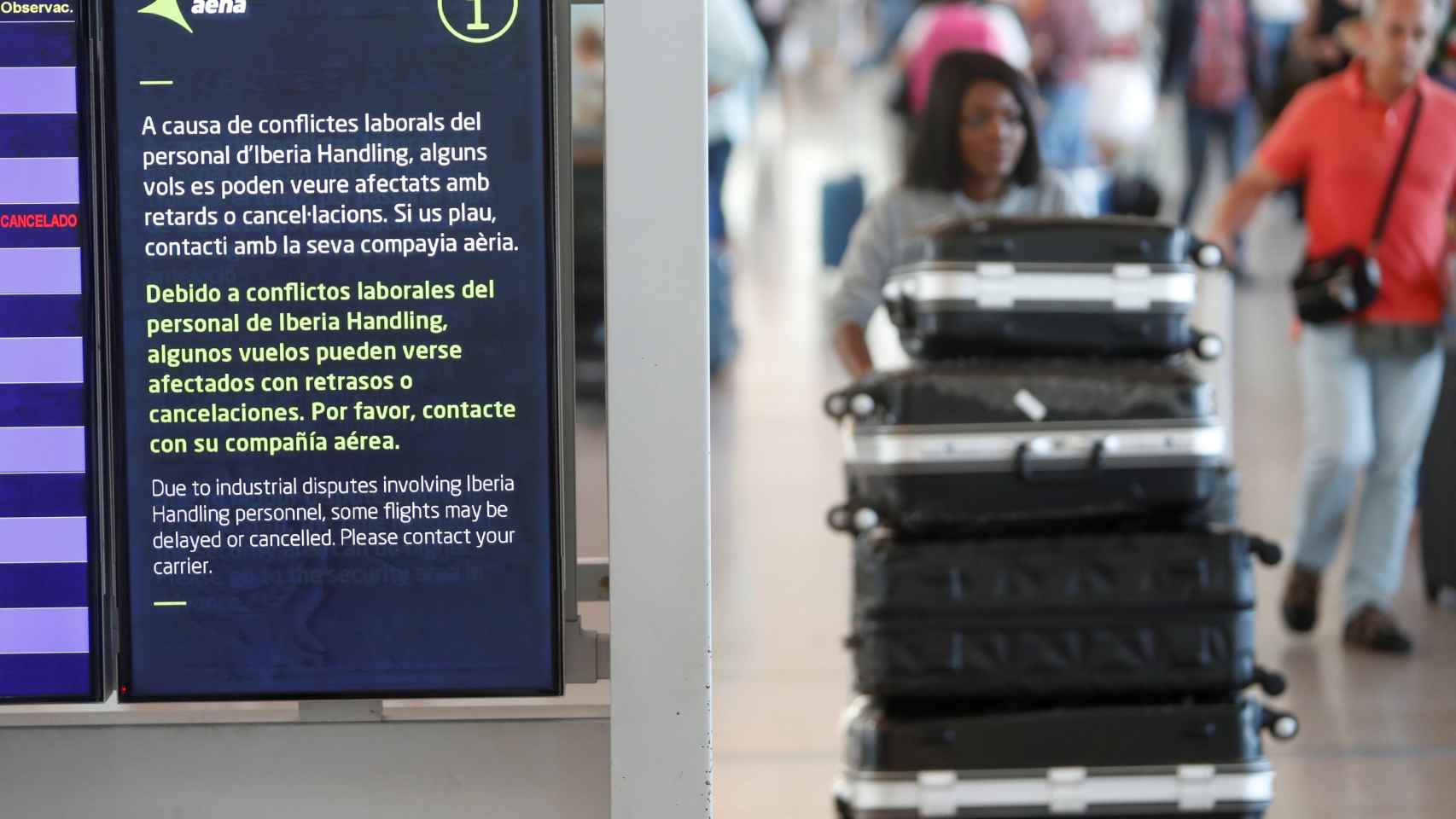 Una mujer con maletas pasa frente a un cartel de Aena en el Aeropuerto de El Prat, donde hay huelga de Iberia / EFE