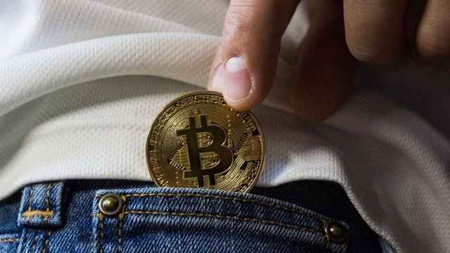 Una persona saca de un bolsillo un bitcoin, una de las criptomonedas más populares / EUROPA PRESS