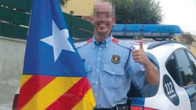 Un mosso d'Esquadra uniformado posa con la bandera independentista ante su coche patrulla / CG