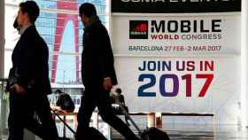 Asistentes al Mobile World Congress del año pasado, arrastrando maletas ante un cartel de la feria / EFE
