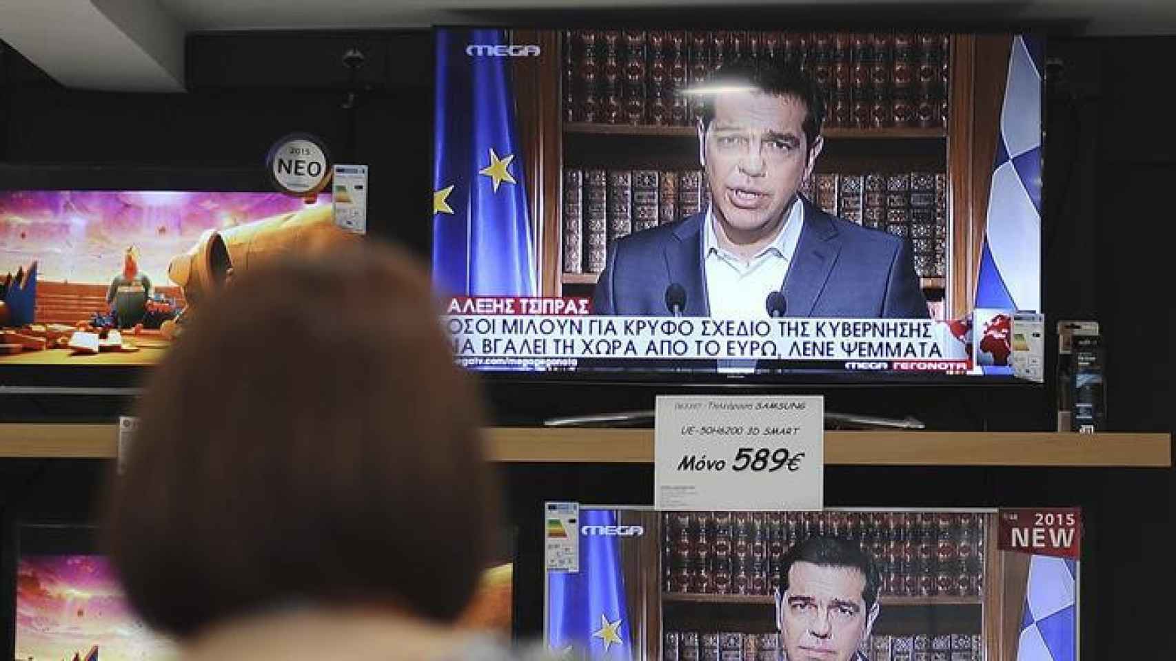 Una ciudadana griega contempla a Tsipras este mediodía en la televisión