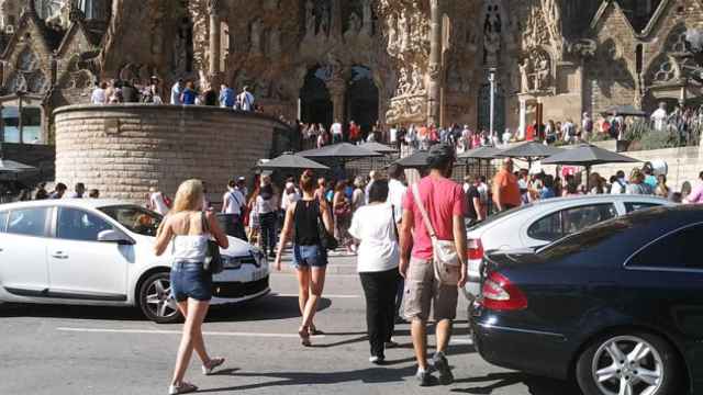 Turistas cruzan pasando entre los coches en la plaza de la Sagrada Familia / CG