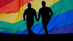 Dos hombres corren con pasividad cogidos de la mano con una bandera LGBTI de fondo / CG