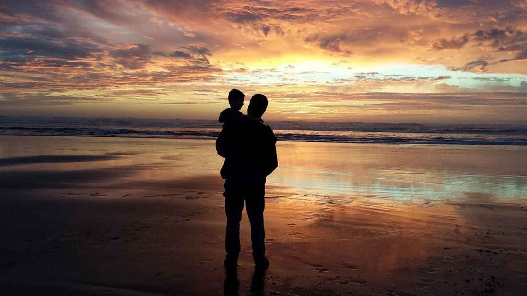 Un padre con su hijo viendo un atardecer en la playa / PIXABAY